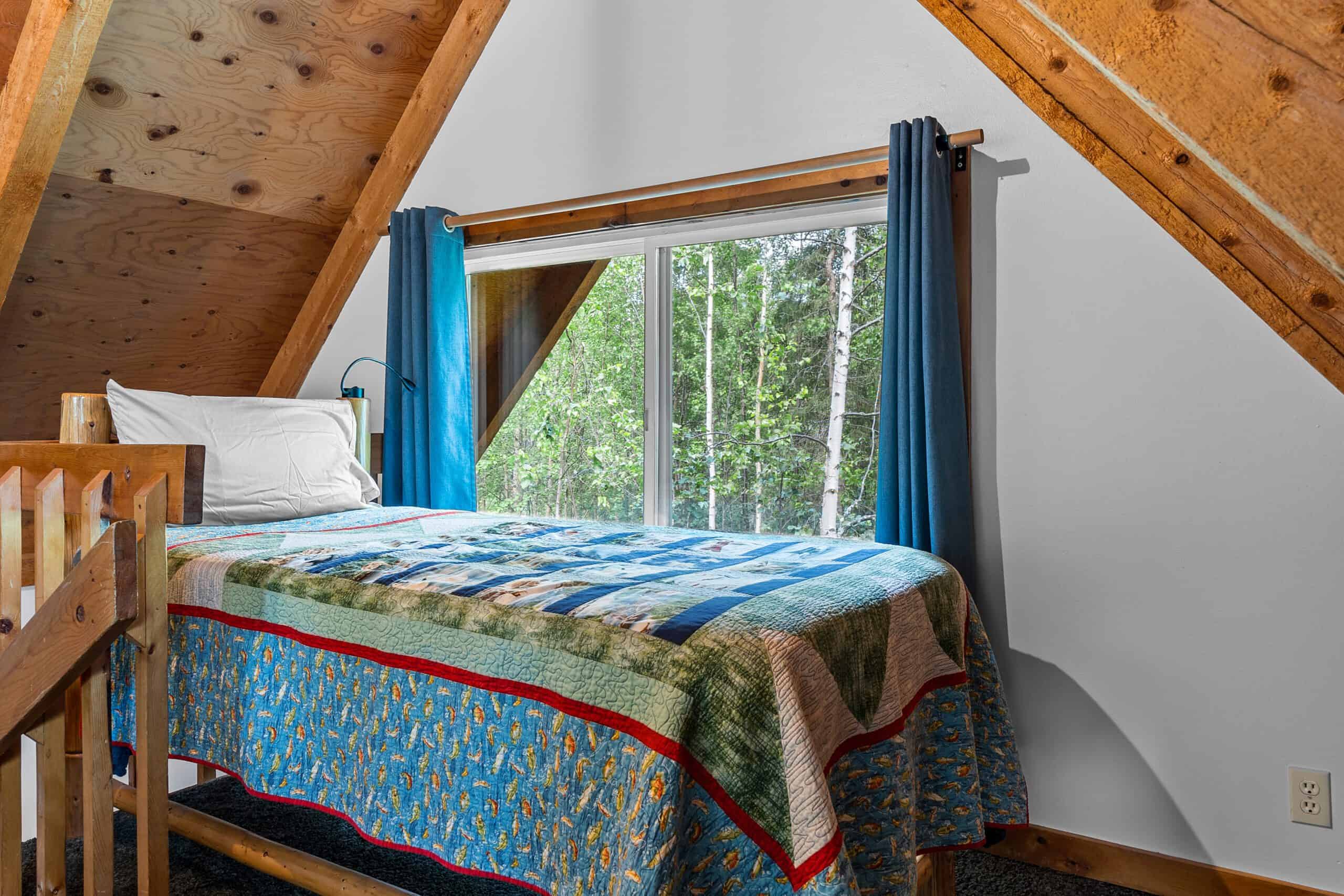 Cozy bedroom with mountain views, wooden accents, and vibrant curtains at Kenai River Drifters Lodge.