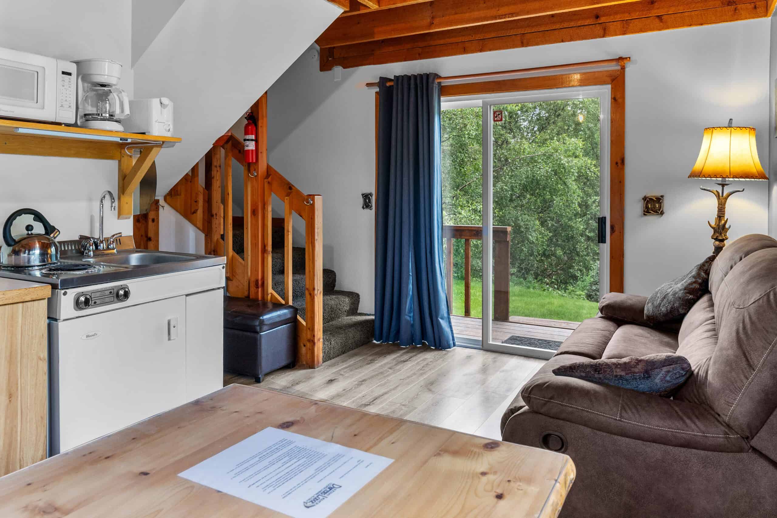 Cozy interior of Kenai River Drifters Lodge with living area and kitchen, wooden accents, and scenic view through glass door.