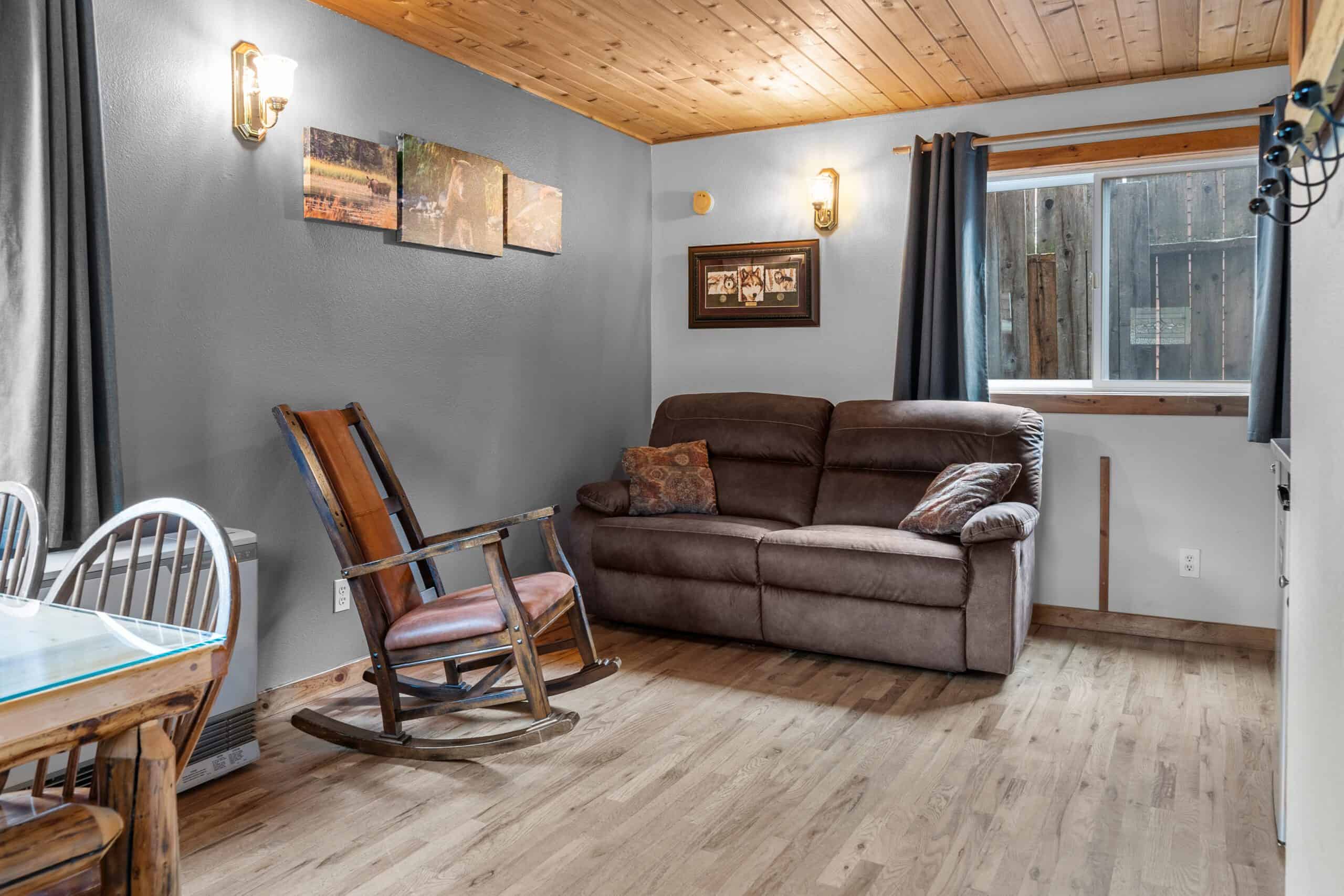 Cozy living room with wooden accents, a brown sofa, and rocking chair at Kenai River Drifters Lodge.