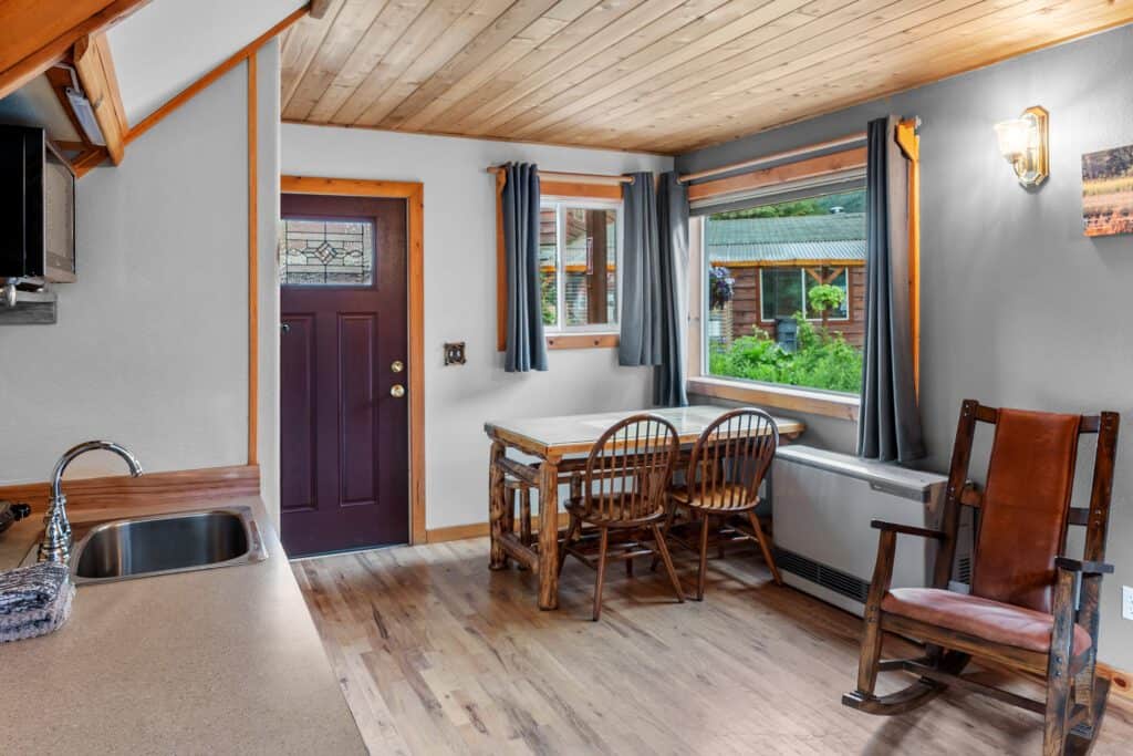 Cozy interior of Kenai River Drifters Lodge with wood accents, dining area, and view of lush greenery outside.