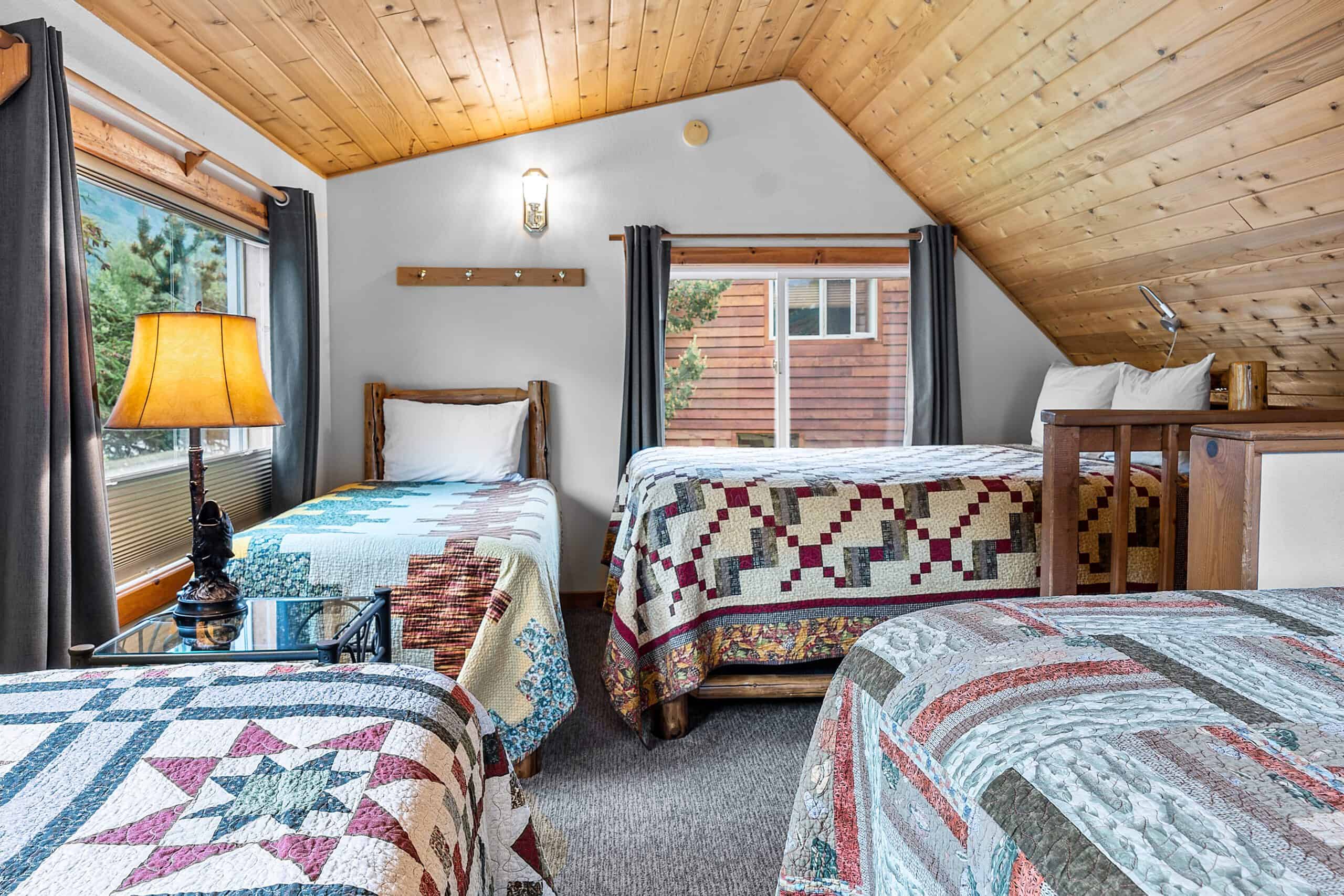 Cozy bedroom with multiple beds, wooden ceiling, and large windows in Kenai River Drifters Lodge.