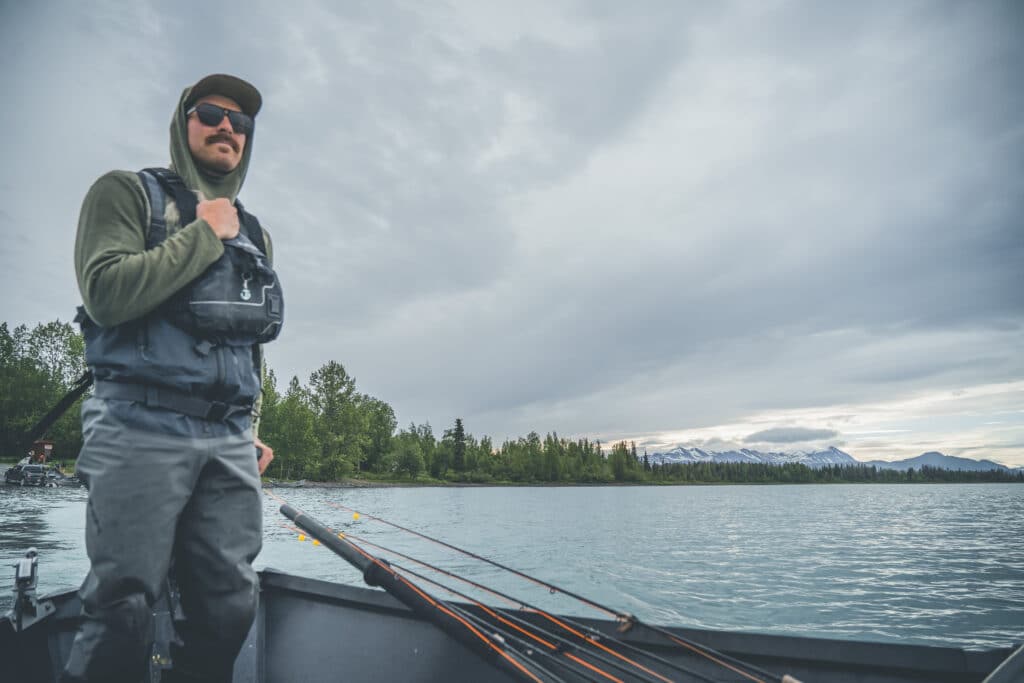 Freshwater fishing on Kenai River with mountains in the background, surrounded by lush trees, under a cloudy sky.