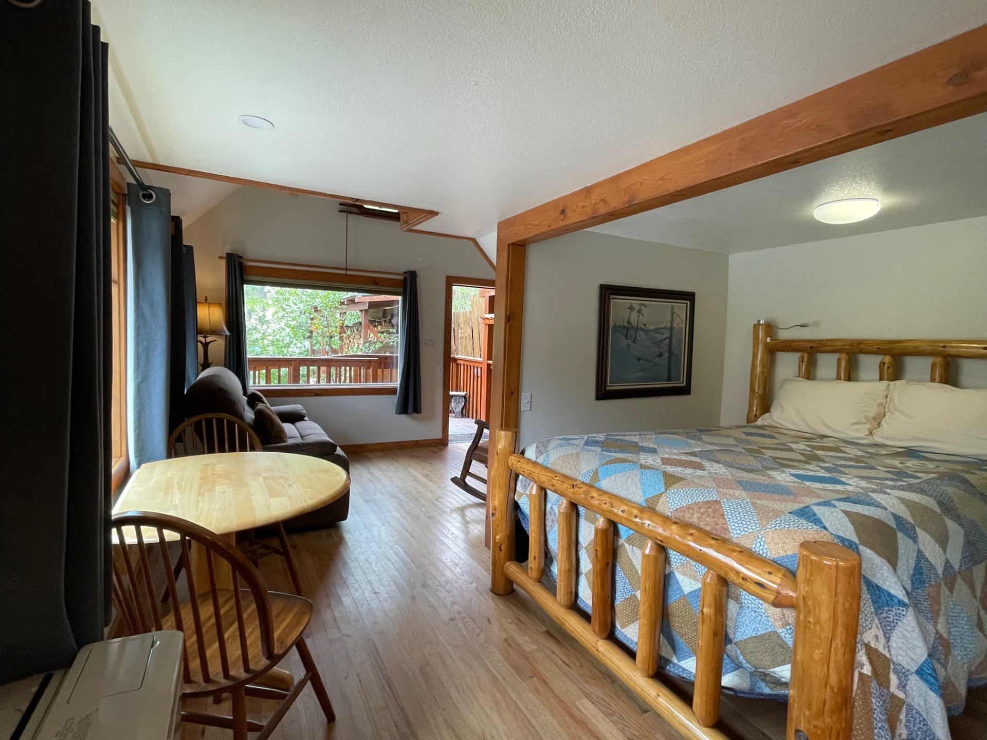 Cozy lodge room with a rustic wooden bed, sitting area, and large windows overlooking nature.