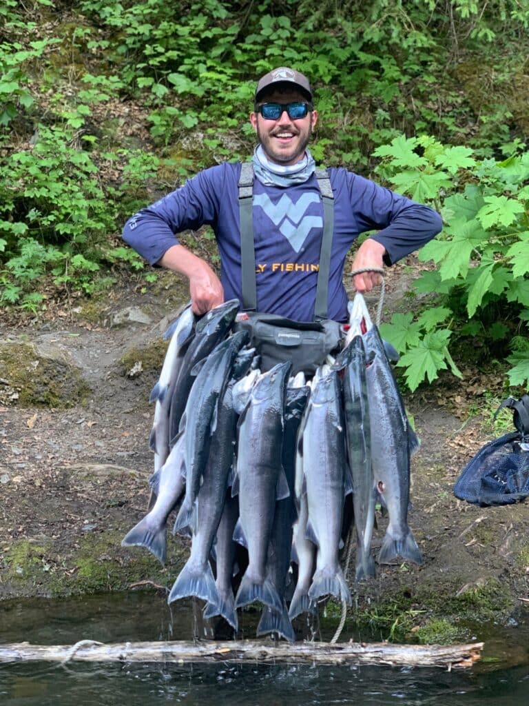Freshly caught salmon hanging from a angler's gear in lush greenery.