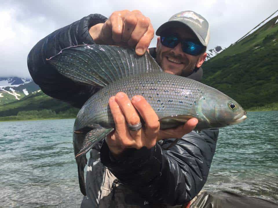 Large fish caught on a fishing trip in Kenai River, Alaska, by a smiling angler wearing sunglasses and a cap.