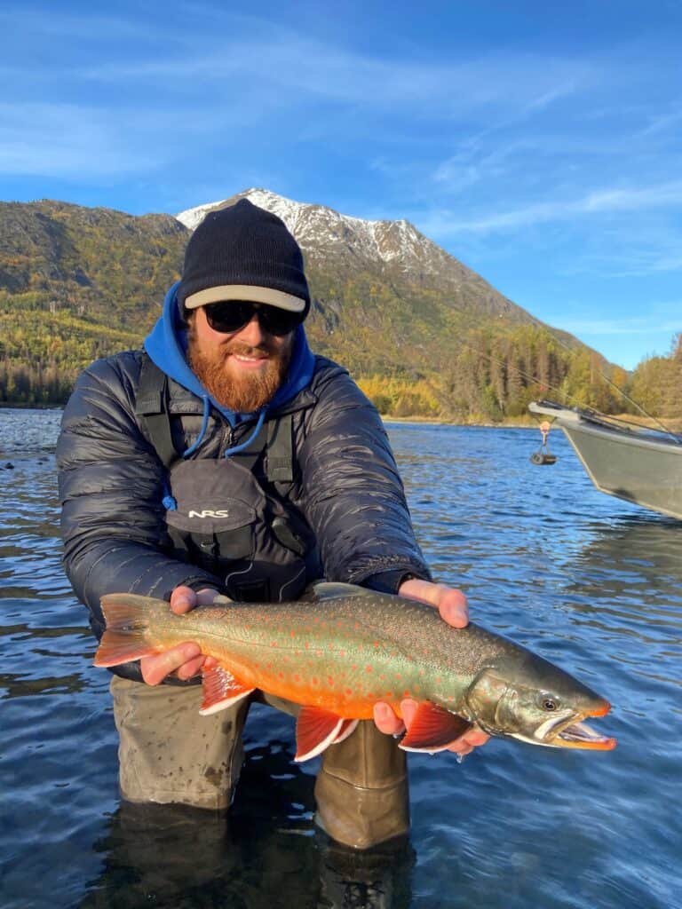 Rainbow trout caught fishing in Kenai River with mountains in the background, clear skies, and vibrant fall foliage.