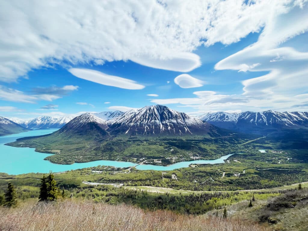 Vibrant landscape of snow-capped mountains, turquoise lakes, and lush green forests near Kenai River Drifters Lodge.