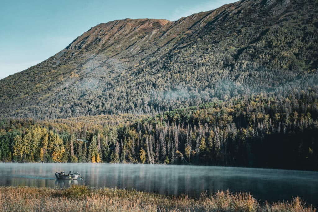 Serene boat on the Kenai River against forested mountains during autumn.