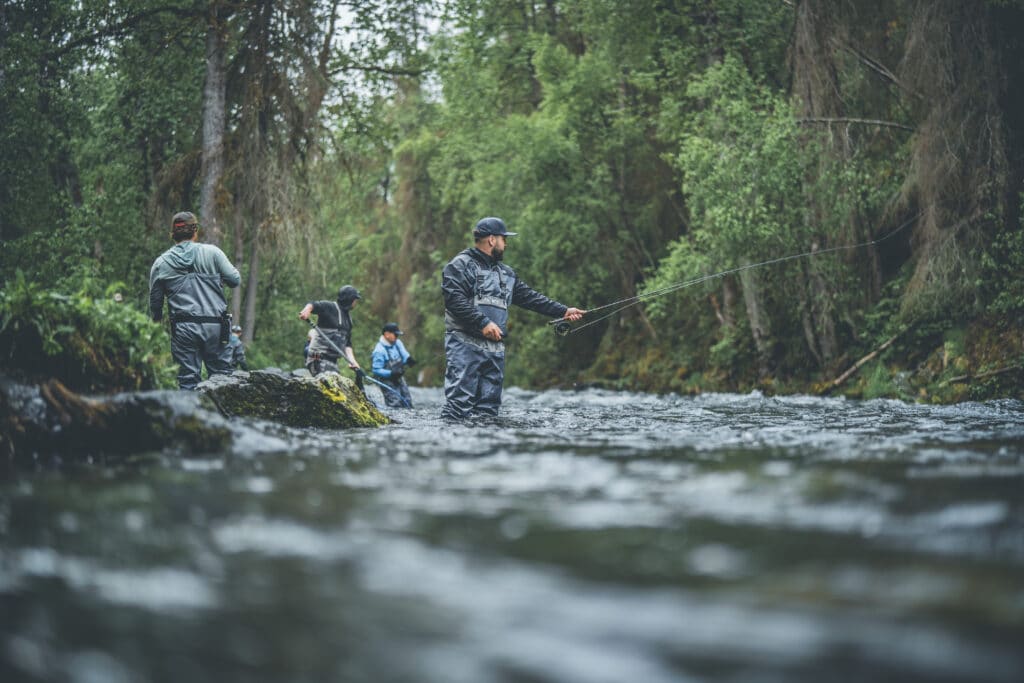 Fishermen safely casting in the Kenai River surrounded by lush green forest.