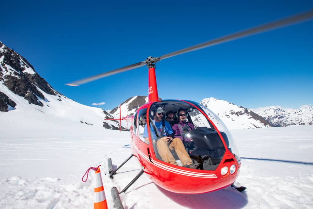 Red helicopter flying over snowy mountains in Alaska for scenic tours.