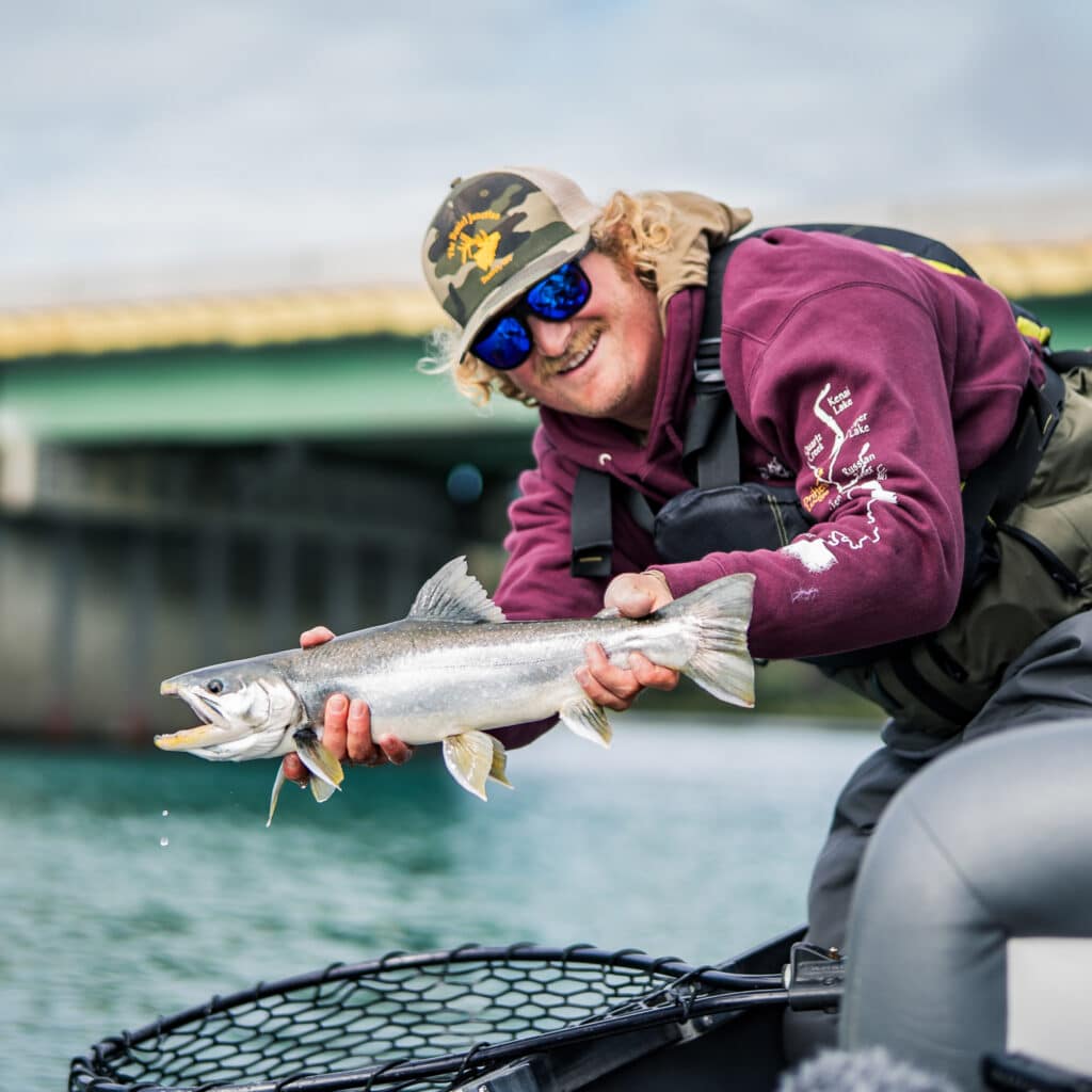 Vibrant image of a smiling man holding a fish after a successful catch at Kenai River Drifters Lodge. Perfect for fishing adventure travelers.
