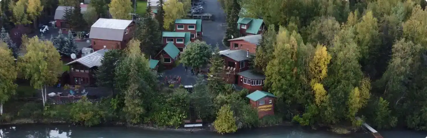 Aerial view of Kenai River Drifters Lodge surrounded by lush fall-colored trees and cozy cabins near the water.