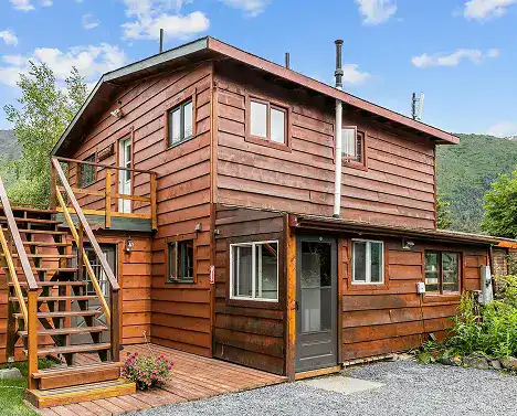Vintage wooden lodge on Kenai River with outdoor staircase and lush mountain backdrop.