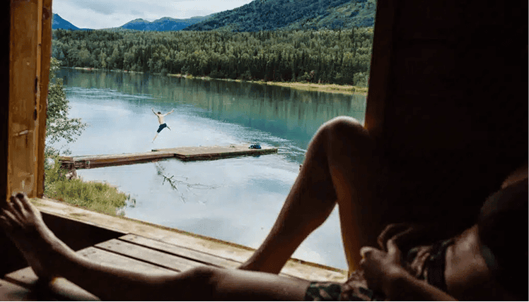 Kenai River view from a cozy lodge window with wilderness scenery and a person relaxing inside.