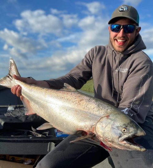 Large Alaskan salmon caught by a smiling angler in outdoor fishing trip.