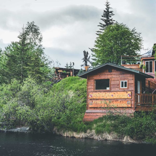 Secluded wooden lodge by the Kenai River surrounded by lush green trees and nature.
