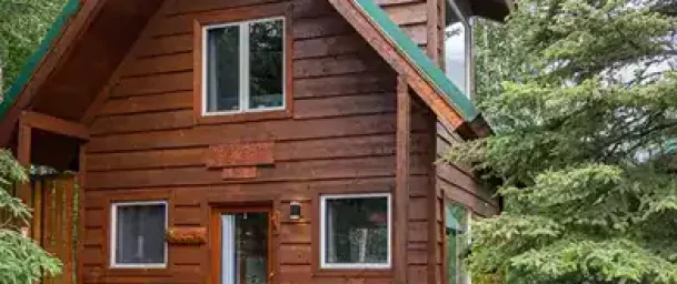 Cozy wooden cabin at Kenai River Drifters Lodge surrounded by lush greenery and tall trees.