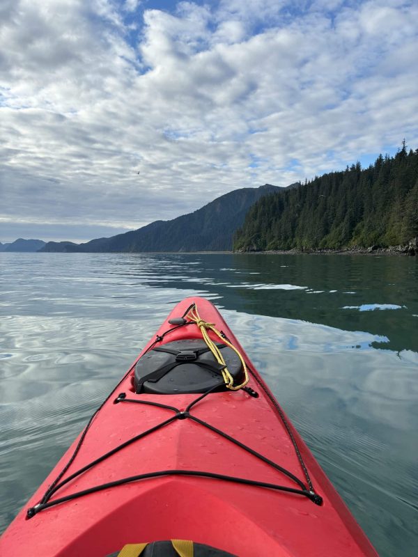 Kayak on calm water with mountain and forest scenery under a partly cloudy sky.