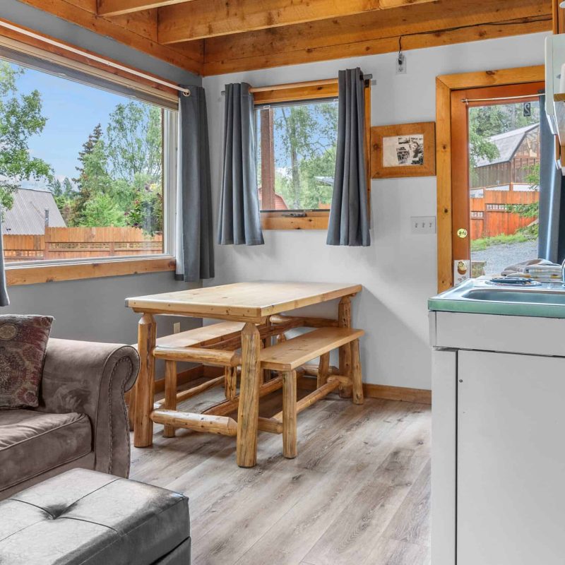 Cozy cabin interior with large windows, wooden accents, and a small kitchenette in Kenai River Drifters Lodge.