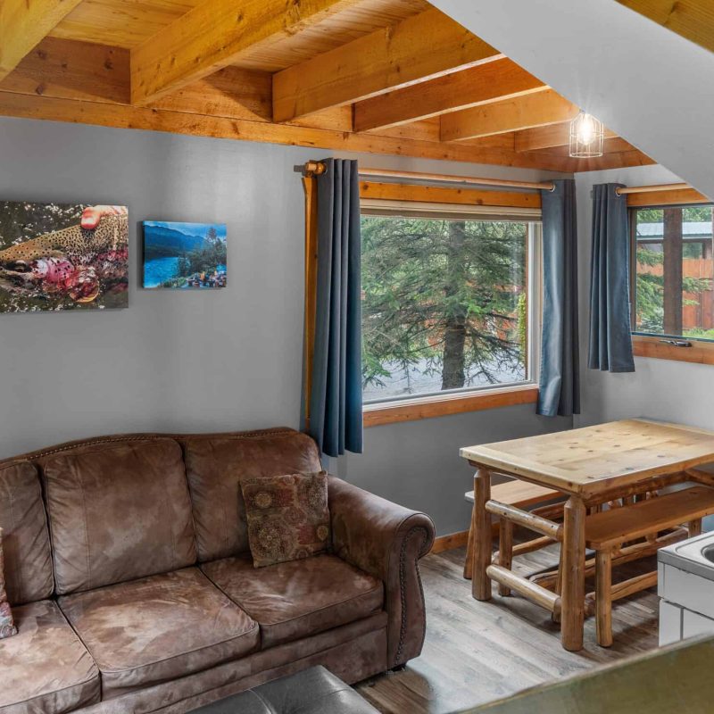Cozy interior of Kenai River Drifters Lodge with rustic wooden accents and large windows showing trees outside.