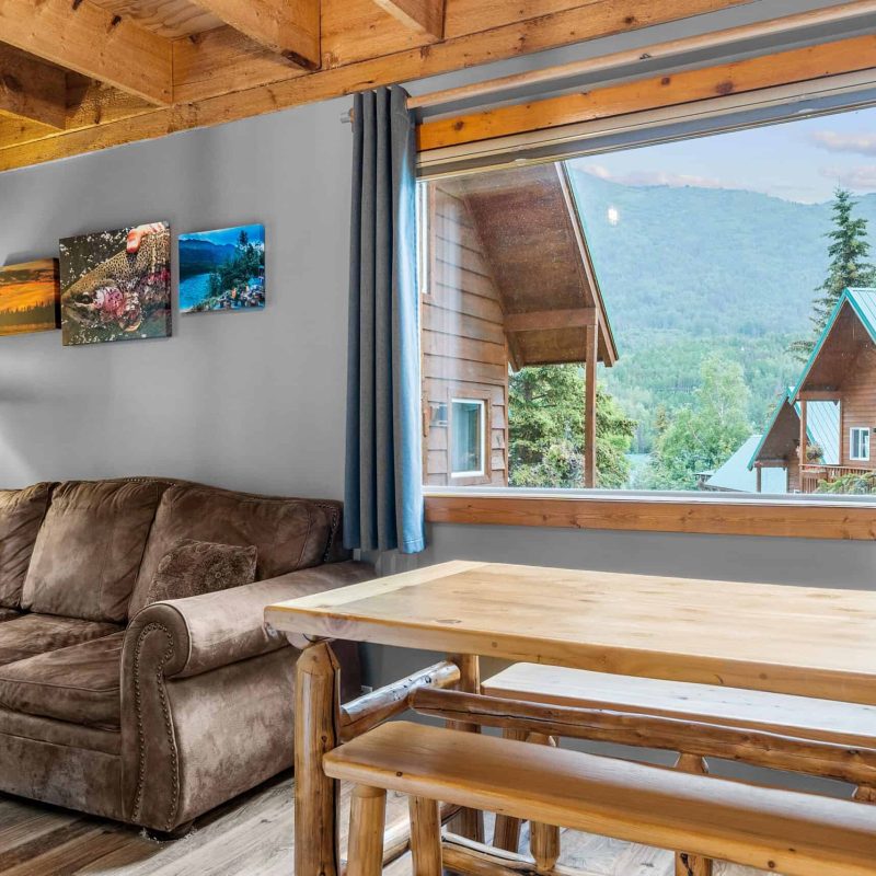 Cozy mountain lodge living room with large window overlooking lush landscape and neighboring cabins.