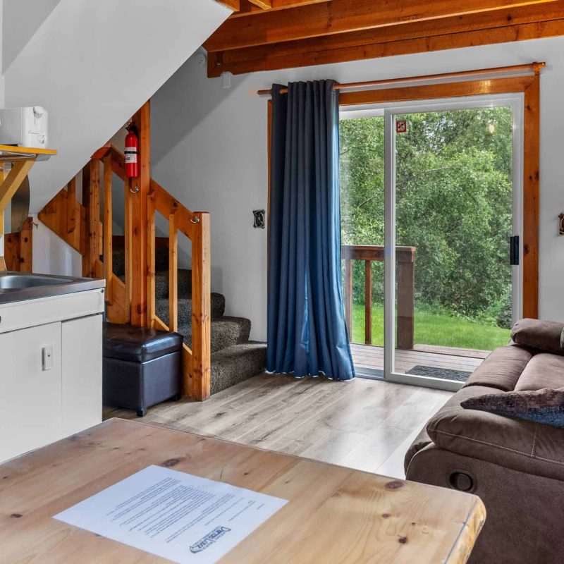 Cozy interior of Kenai River Drifters Lodge with living area and kitchen, wooden accents, and scenic view through glass door.