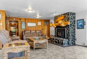 Cozy lodge living room with wooden paneling, stone fireplace, and rustic wood accents.