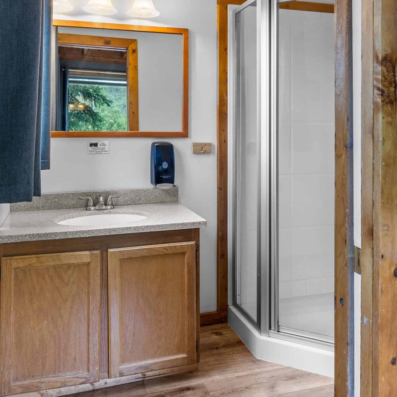 Clean bathroom with wooden cabinets, mirror, and shower at Kenai River Drifters Lodge.