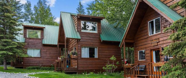 Cozy wooden cabins with green metal roofs surrounded by lush greenery at Kenai River Drifters Lodge.