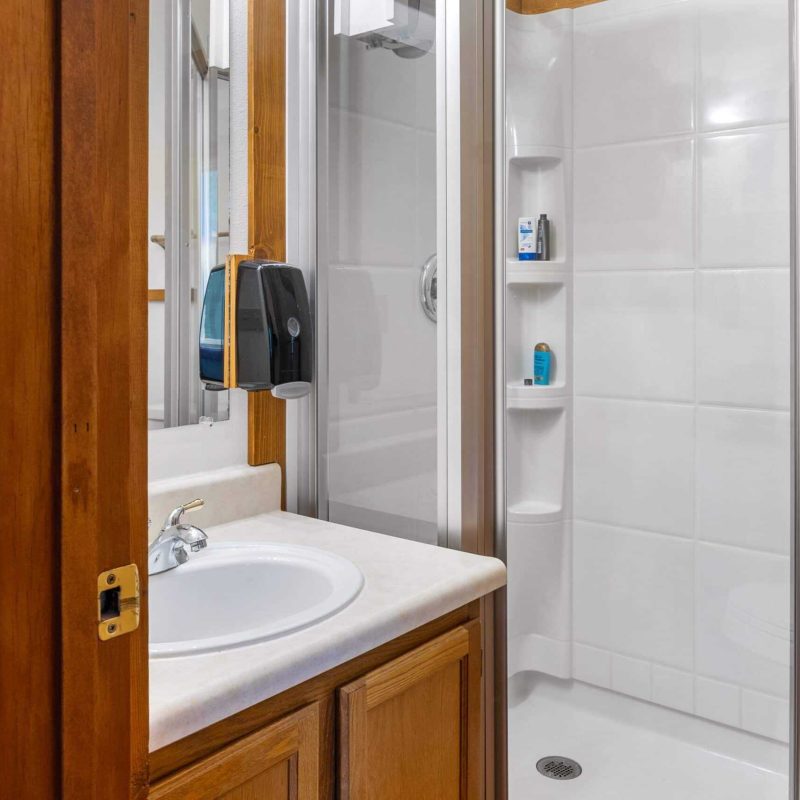 Clean bathroom with shower, sink, and wooden accents at Kenai River Drifters Lodge, Alaska.