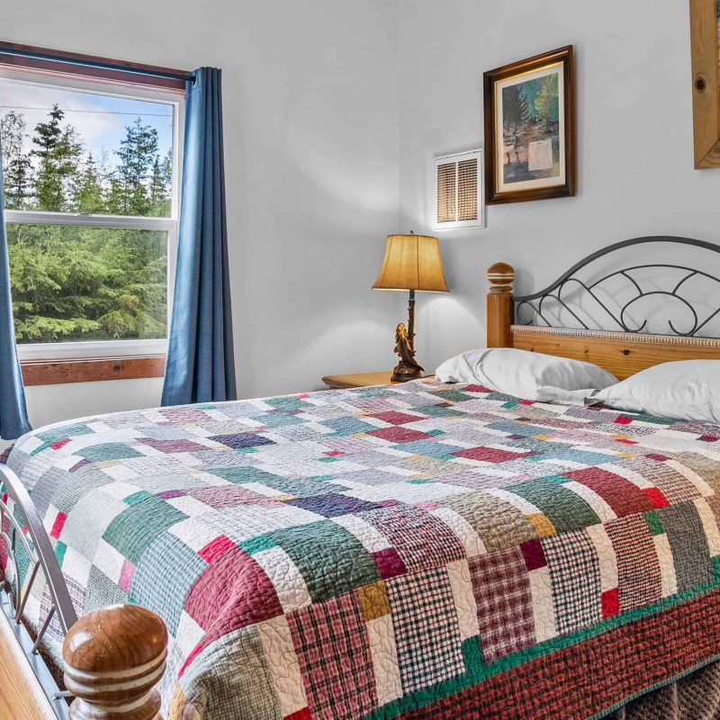Cozy bedroom with colorful quilt, wooden furniture, and natural light at Kenai River Drifters Lodge.