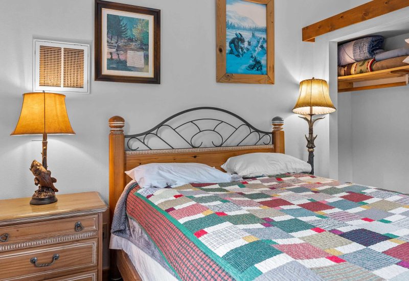 Cozy bedroom with rustic décor and a colorful patchwork quilt at Kenai River Drifters Lodge, featuring wooden furniture and nature-themed artwork.