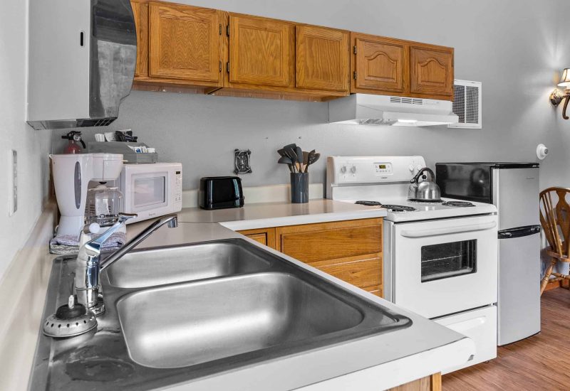 Clean kitchen with stainless steel sink, white appliances, wooden cabinets in Kenai River Drifters Lodge.