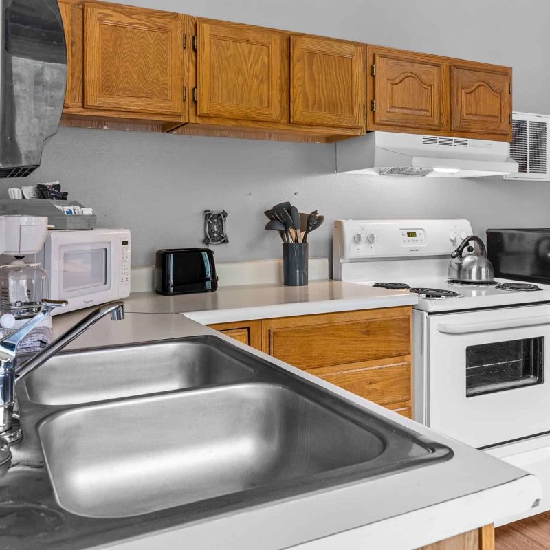 Clean kitchen with stainless steel sink, white appliances, wooden cabinets in Kenai River Drifters Lodge.