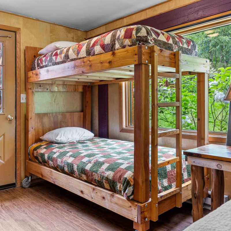 Cozy bunk bedroom with rustic wooden furniture and vibrant checkered bedding at Kenai River Drifters Lodge.