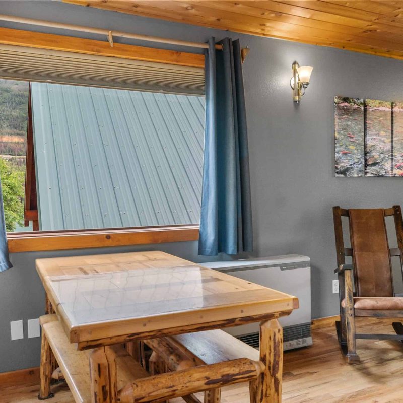 Cozy indoor space at Kenai River Drifters Lodge, featuring a wooden dining table, rocking chair, and mountain views through the window.