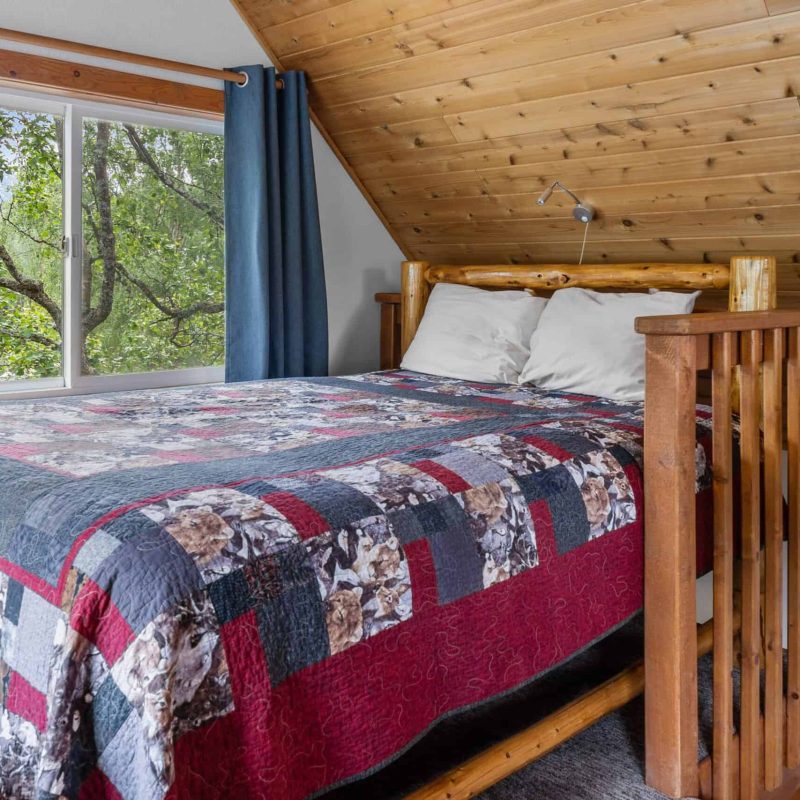 Cozy rustic bedroom with log bed and scenic window view of trees, perfect for Kenai River Lodging.