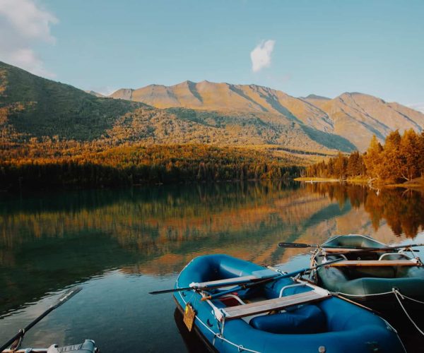 Boats on Kenai River with mountain and forest backdrop at sunset.