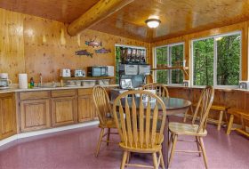 Cozy wooden cabin kitchen with natural light and forest views, featuring a round dining table and rustic decor.