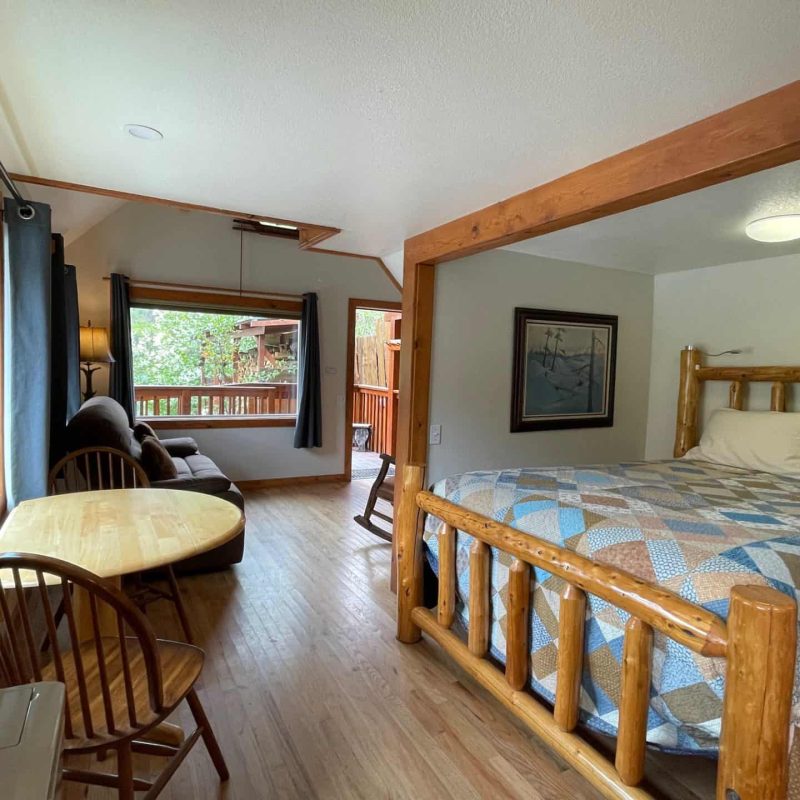Cozy lodge room with a rustic wooden bed, sitting area, and large windows overlooking nature.