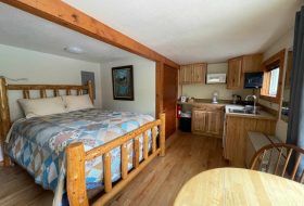 Cozy rustic cabin interior featuring a wooden bed, small kitchen, and dining area at Kenai River Drifters Lodge.