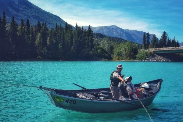 Fishing boat on turquoise river surrounded by dense forest and mountains near Kenai River Drifters Lodge.