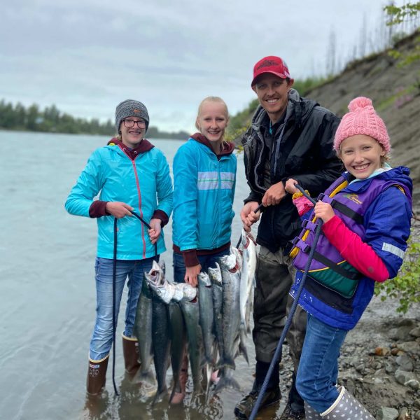 Fishing family with caught salmon along Kenai River, Alaska, during a driftnet fishing adventure.