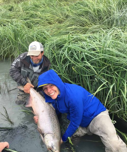 Angler smiling and holding a large king salmon caught while Alaska fishing in June on the Kenai River.