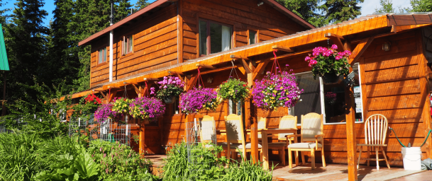 Colorful wooden lodge with hanging flower baskets and outdoor seating amid lush greenery at Kenai River Drifters Lodge.